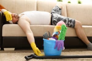 Man asleep on couch wearing clean gloves and cleaning supplies near. 