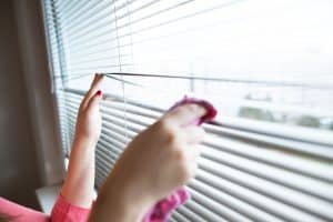 Hand of young woman cleaning blinds by pink cloth