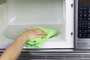 Hand with microfiber cleaning rag wiping inside of microwave oven