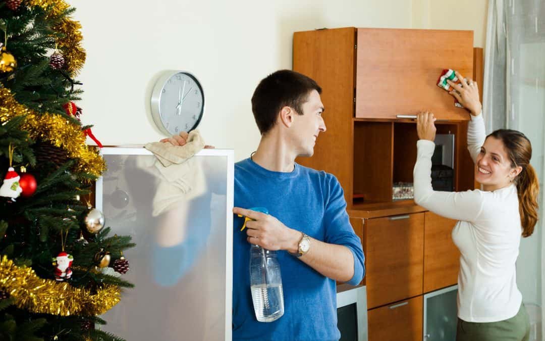 Smiling couple wiping dust from wooden furniture at home in Christmas time