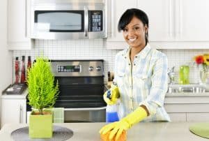 Smiling young black woman with sponge and rubber gloves cleaning kitchen